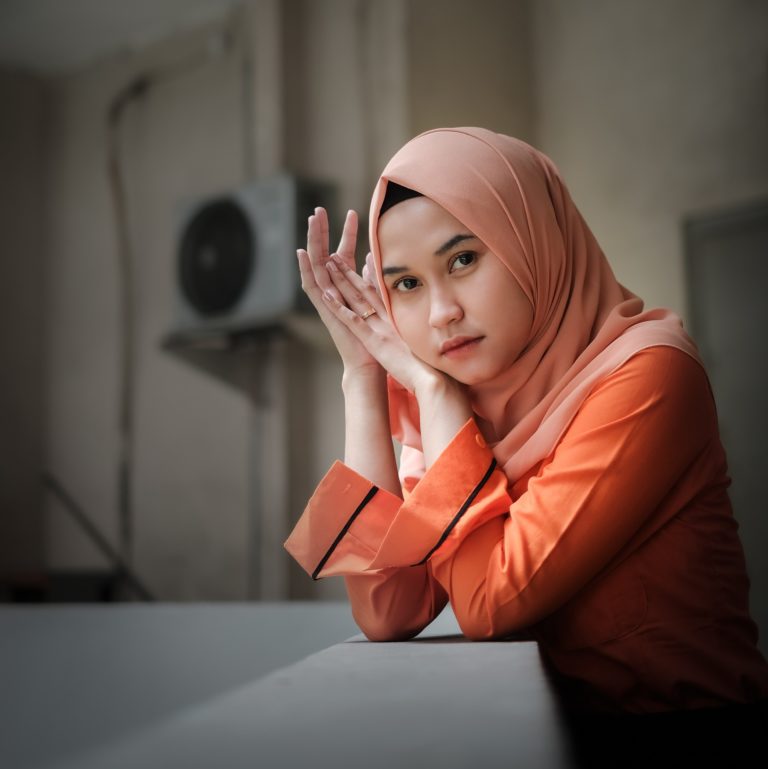 woman wearing a hijab sitting at a desk looking thoughtful